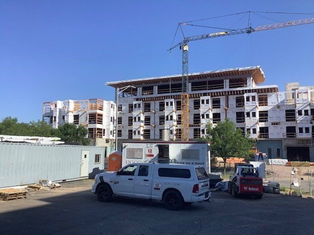 Construction site with crane, partially built buildings, white truck, and machinery under blue sky.