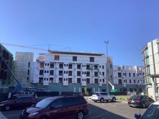 Construction site with buildings under construction, cranes, cars, and a clear blue sky.