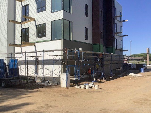 Building exterior under construction with scaffolding. Workers are present. Blue sky overhead.