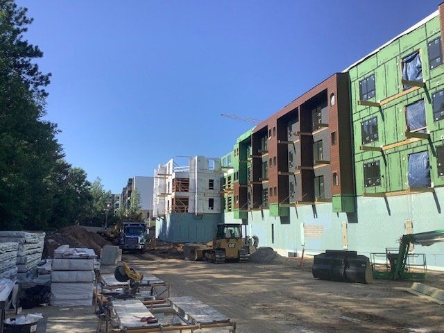 Construction site with multi-story buildings, blue sky. Equipment and materials in foreground.