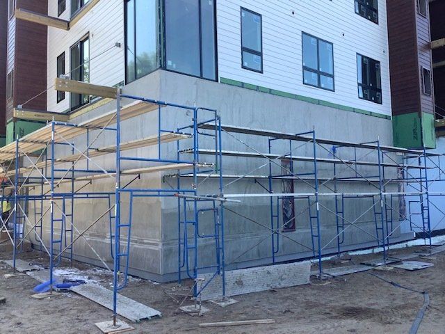 Blue scaffolding around a building under construction. Concrete wall, white siding, and windows are visible.