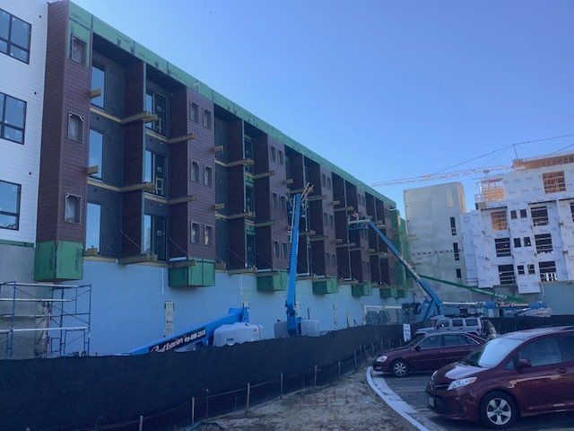 Construction site; multi-story building under construction with blue sky, crane, and parked cars.