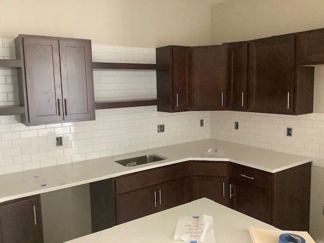 Kitchen with dark brown cabinets, white countertops and backsplash.