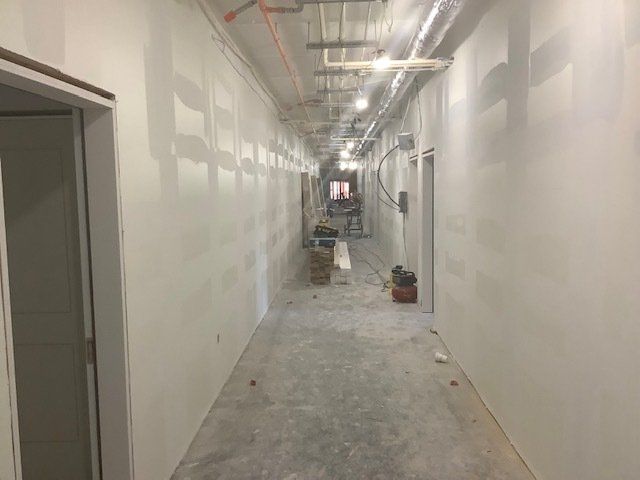 Construction of a hallway, with unfinished drywall and exposed pipes.