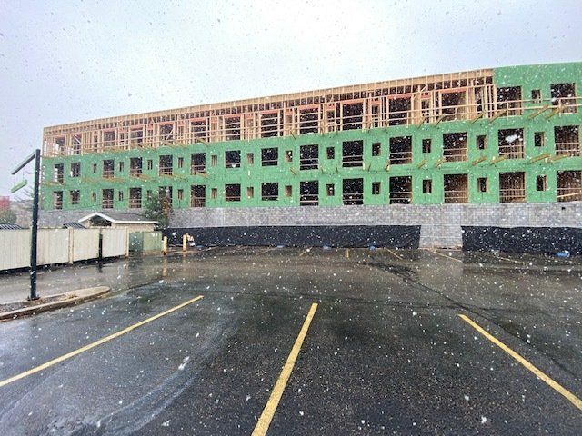 Building under construction on a rainy day with a parking lot in the foreground.