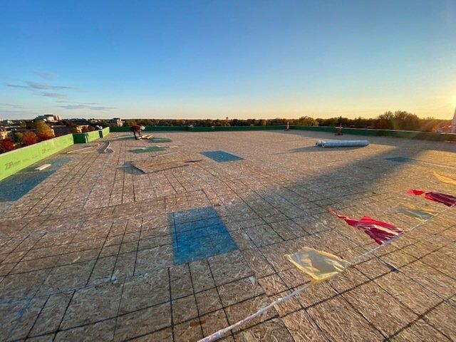 Rooftop with insulation being installed; construction worker, roll of material, and vibrant sky.
