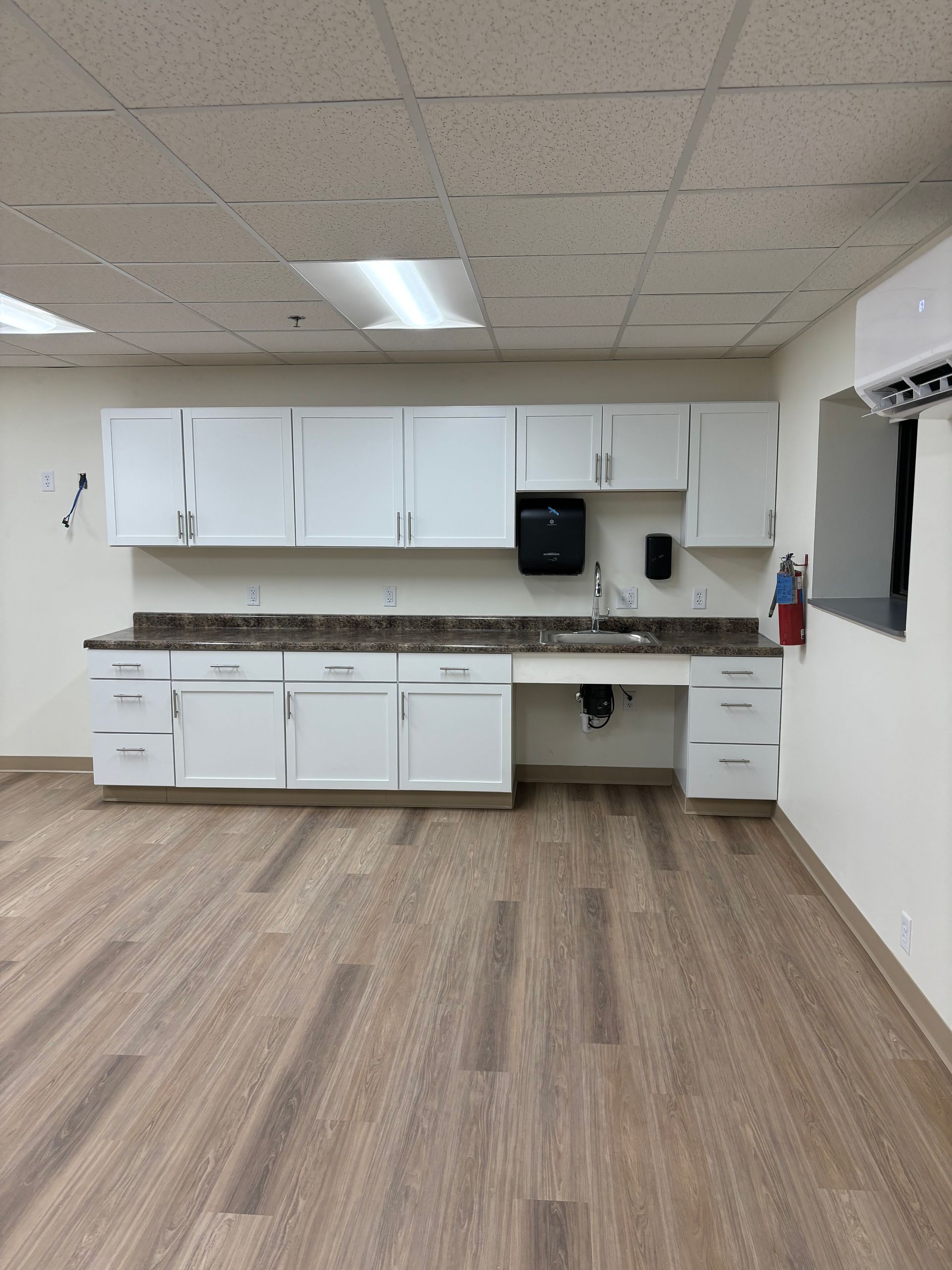 White cabinets above and below a sink. Light brown flooring. A fire extinguisher is visible.