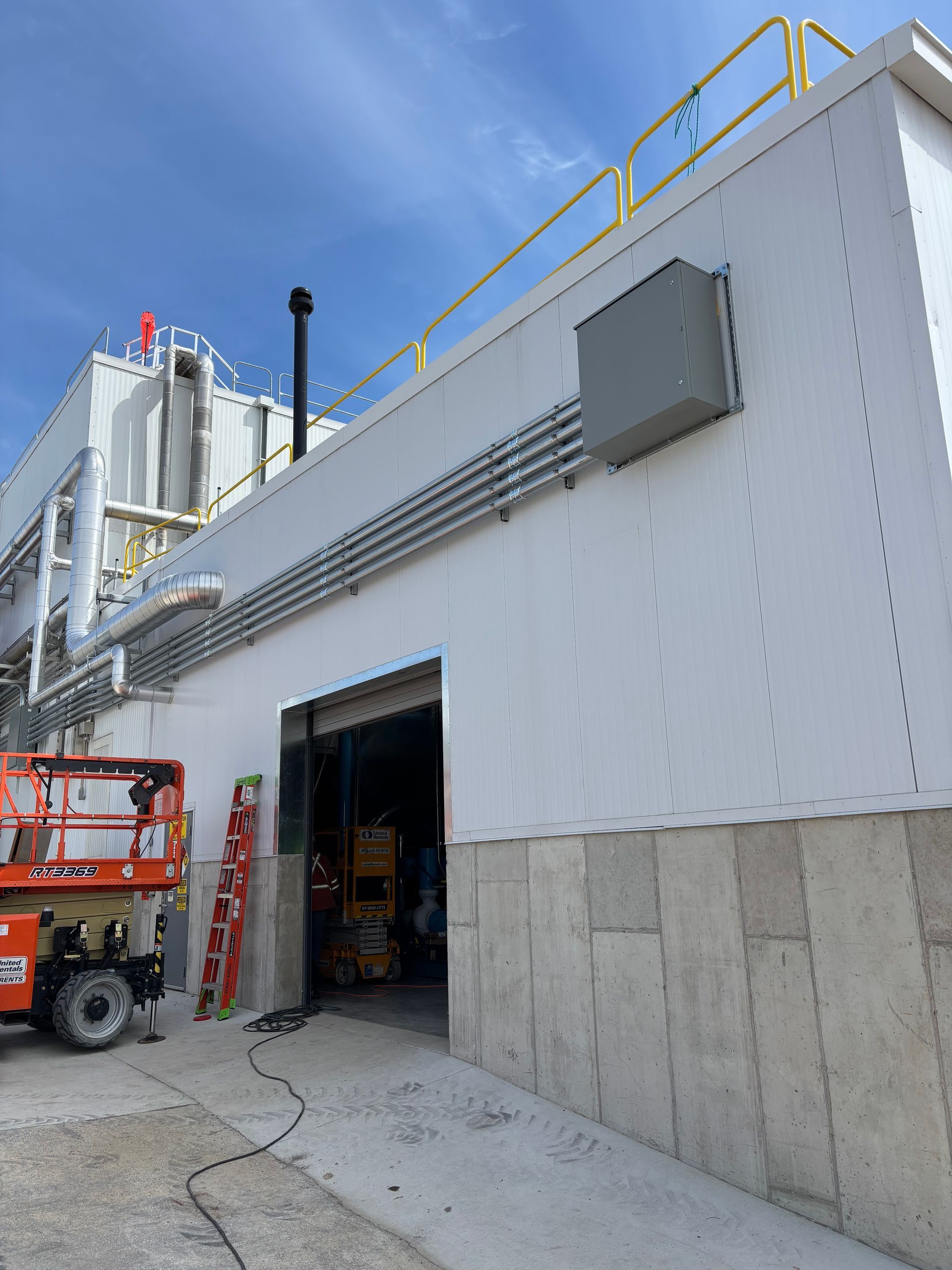 Exterior of an industrial building with a red lift truck and open loading bay under a blue sky