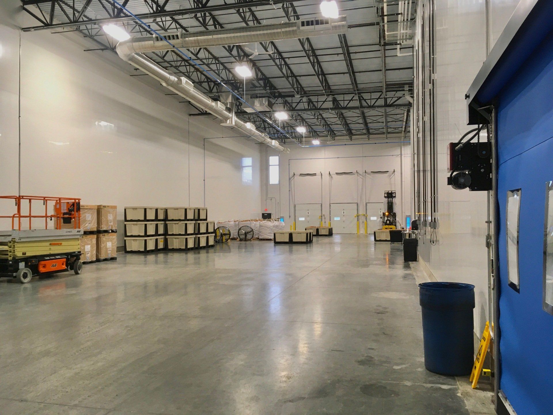 Empty warehouse with boxes, forklift, and loading docks. Blue door on the right.