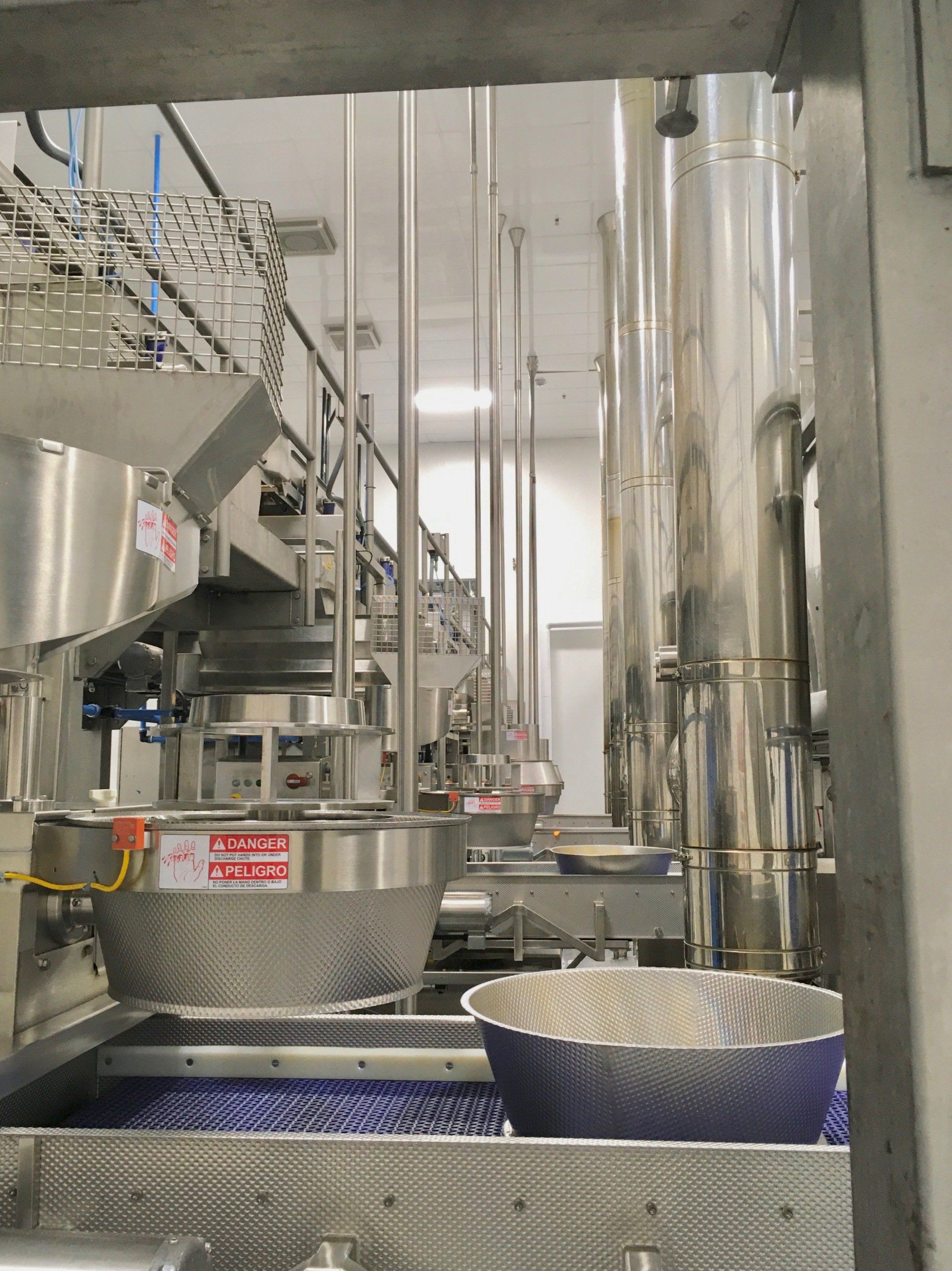 Food processing facility with stainless steel equipment and cylindrical tanks. A conveyor belt is visible.