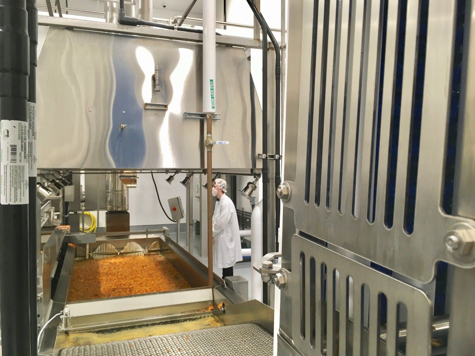 Person in lab coat in a food processing area with stainless steel machinery and containers.