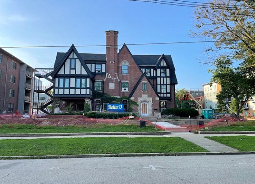 Tudor-style building with black and white accents. Construction fencing surrounds the yard. Blue sky background.