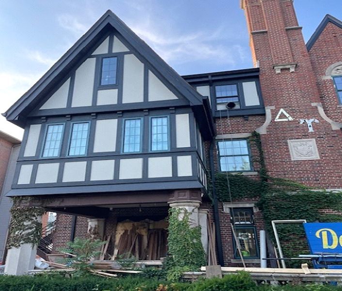 Exterior of a Tudor-style building undergoing renovation, featuring black and white accents, brickwork, and visible construction materials.