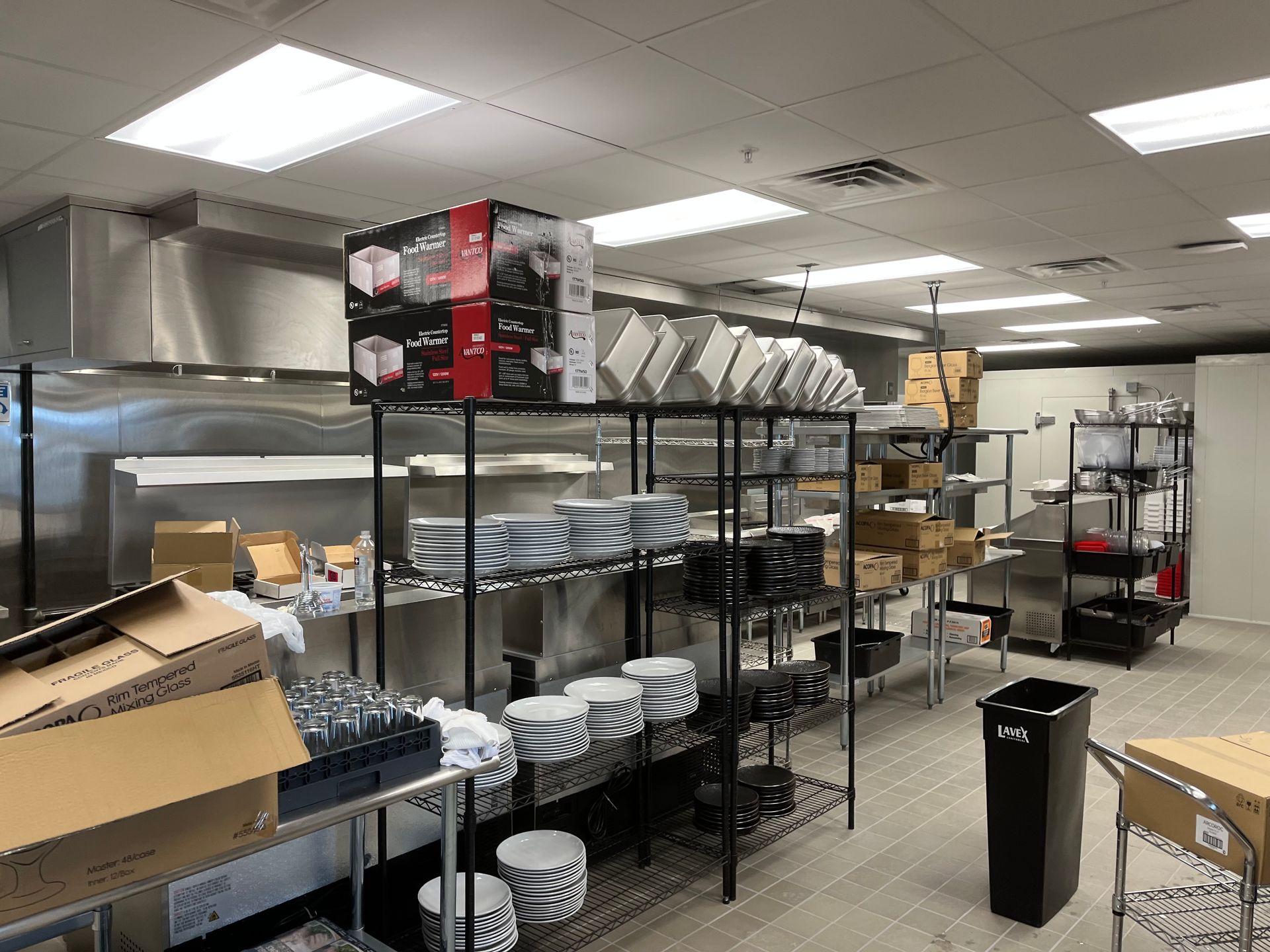 Commercial kitchen interior with stainless steel appliances, shelving holding dishes and supplies.