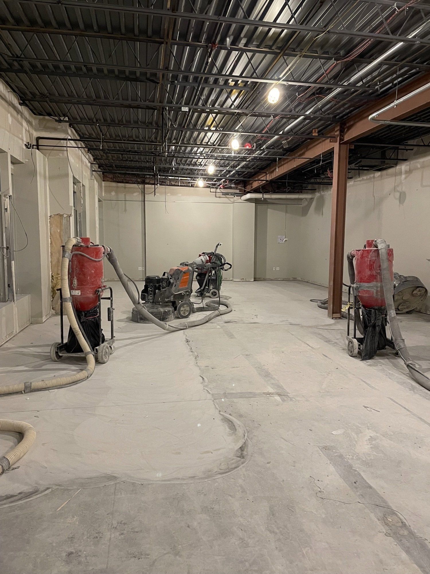 Construction site with concrete floor and multiple dust extraction machines. Exposed ceiling with metal beams and lighting.
