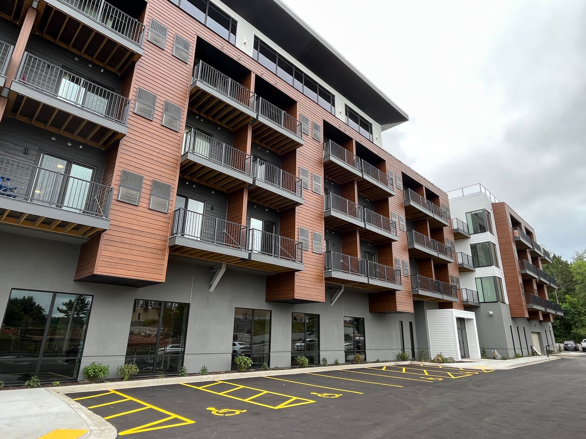 Modern multi-story apartment building with bronze and gray facade, balconies, and ground-level parking.