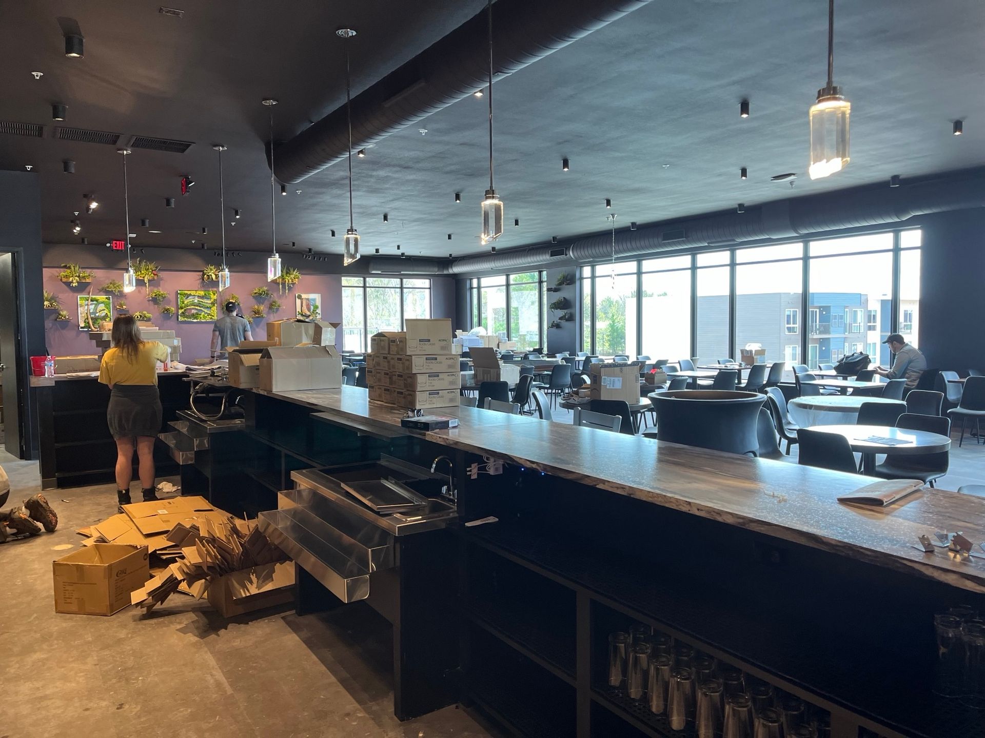 Interior of a restaurant under construction with bar, tables, and a person near the bar.