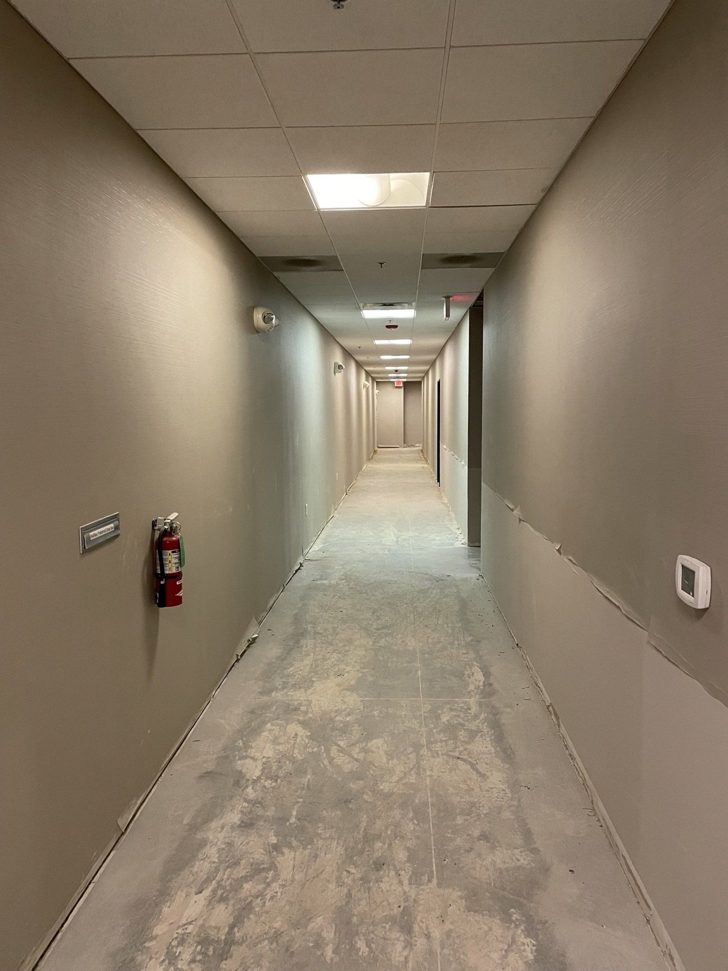 Empty hallway with freshly painted walls, several ceiling lights, and fire extinguisher.