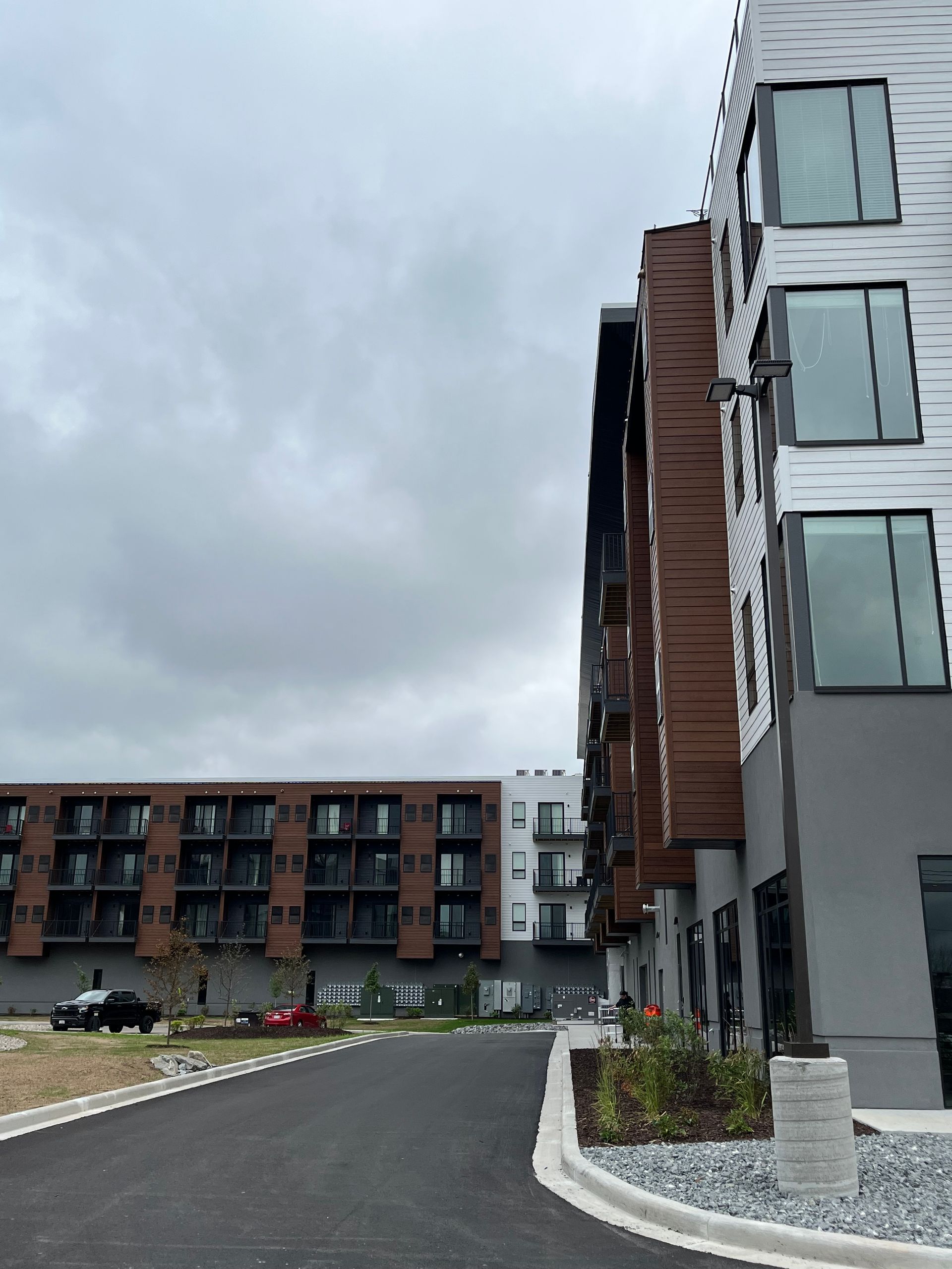 Modern apartment buildings with a dark asphalt driveway under a cloudy sky.
