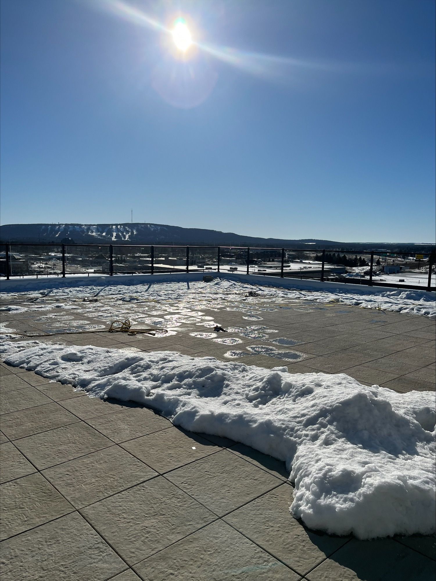 Snow-covered rooftop on a sunny day. Mountain in the distance, clear blue sky.