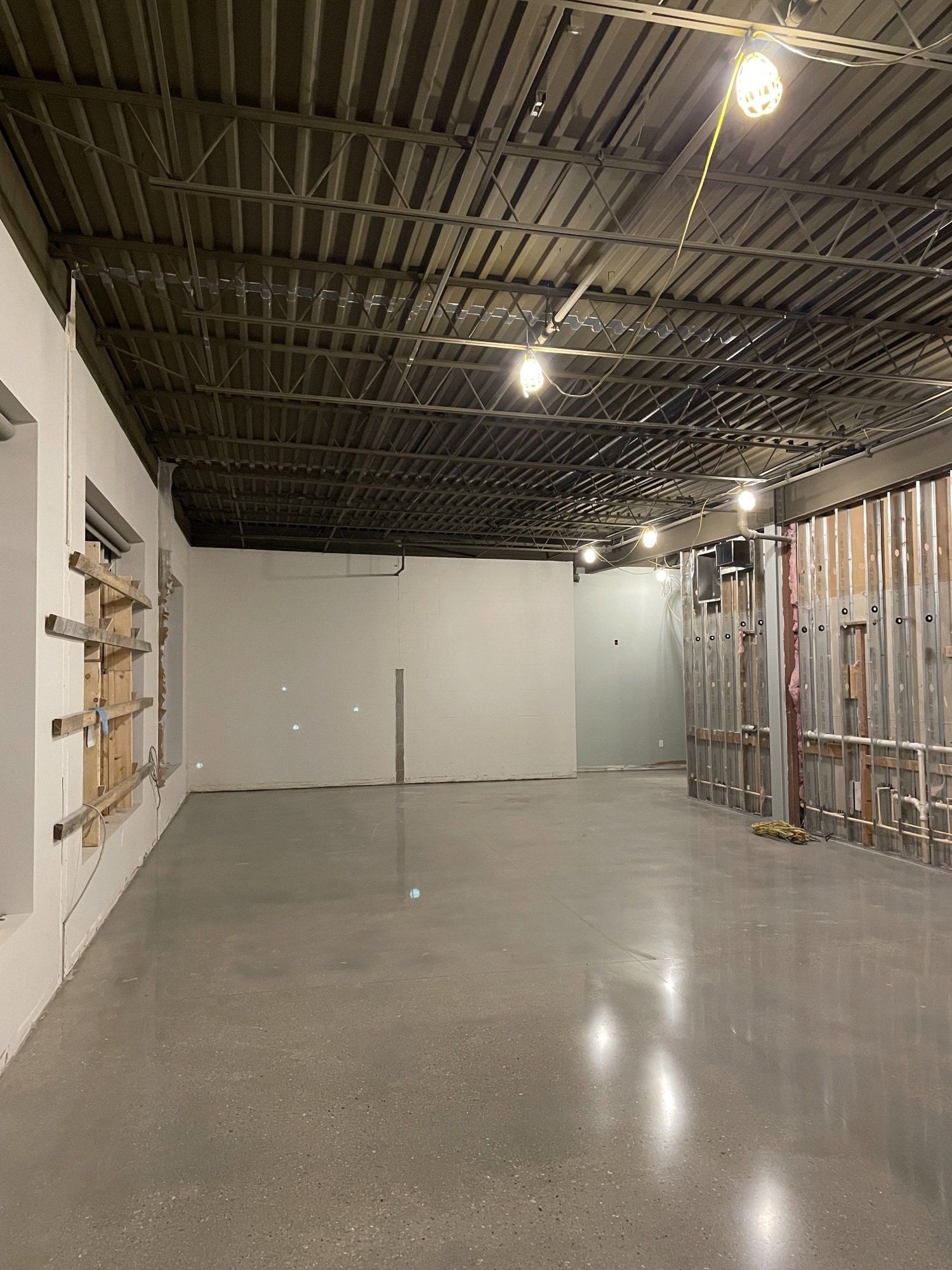 Empty interior space with a concrete floor, metal ceiling, and exposed wall framing.