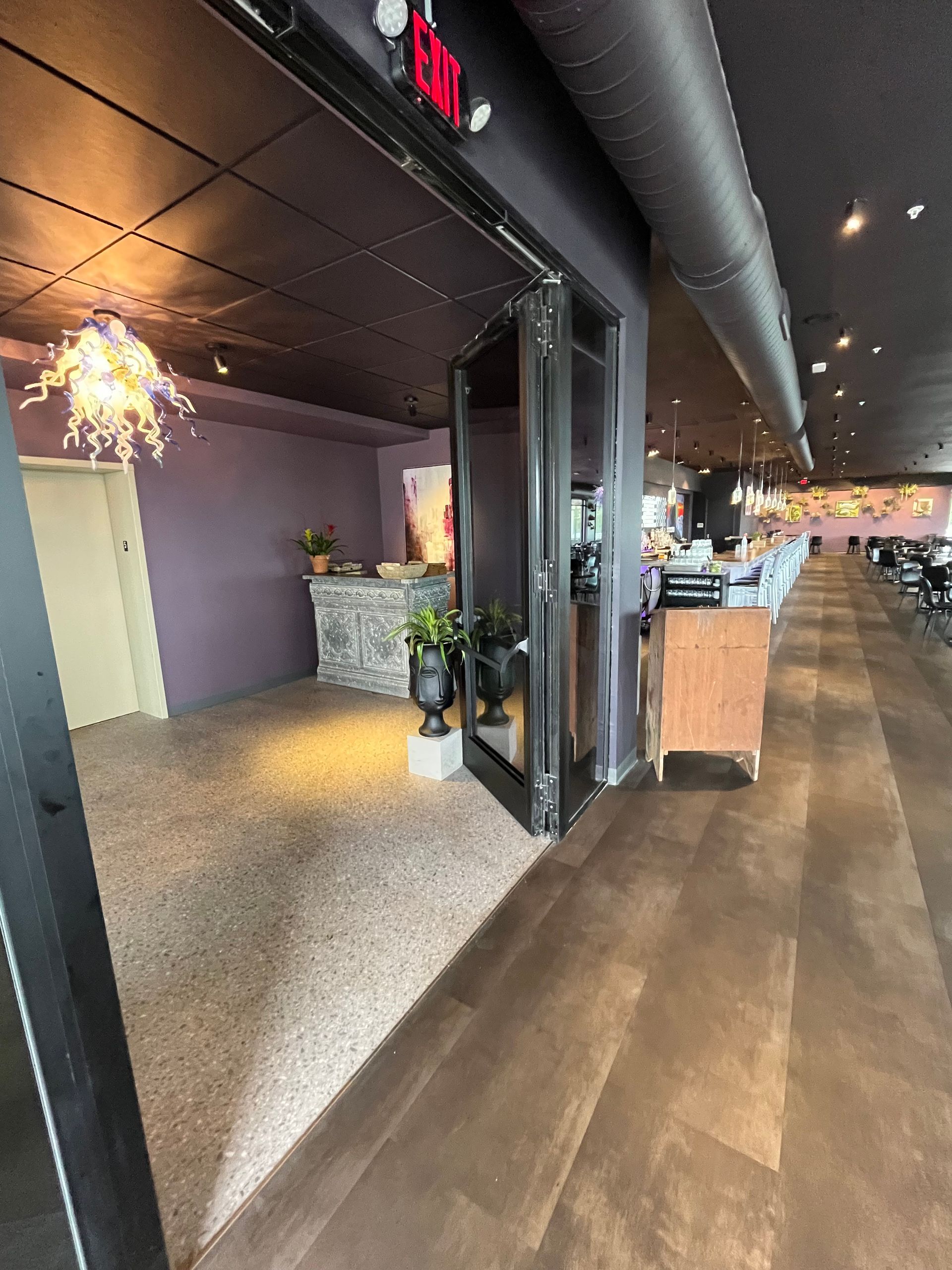 Entrance to a restaurant. Glass doors open to a reception area with purple walls and a decorative countertop.