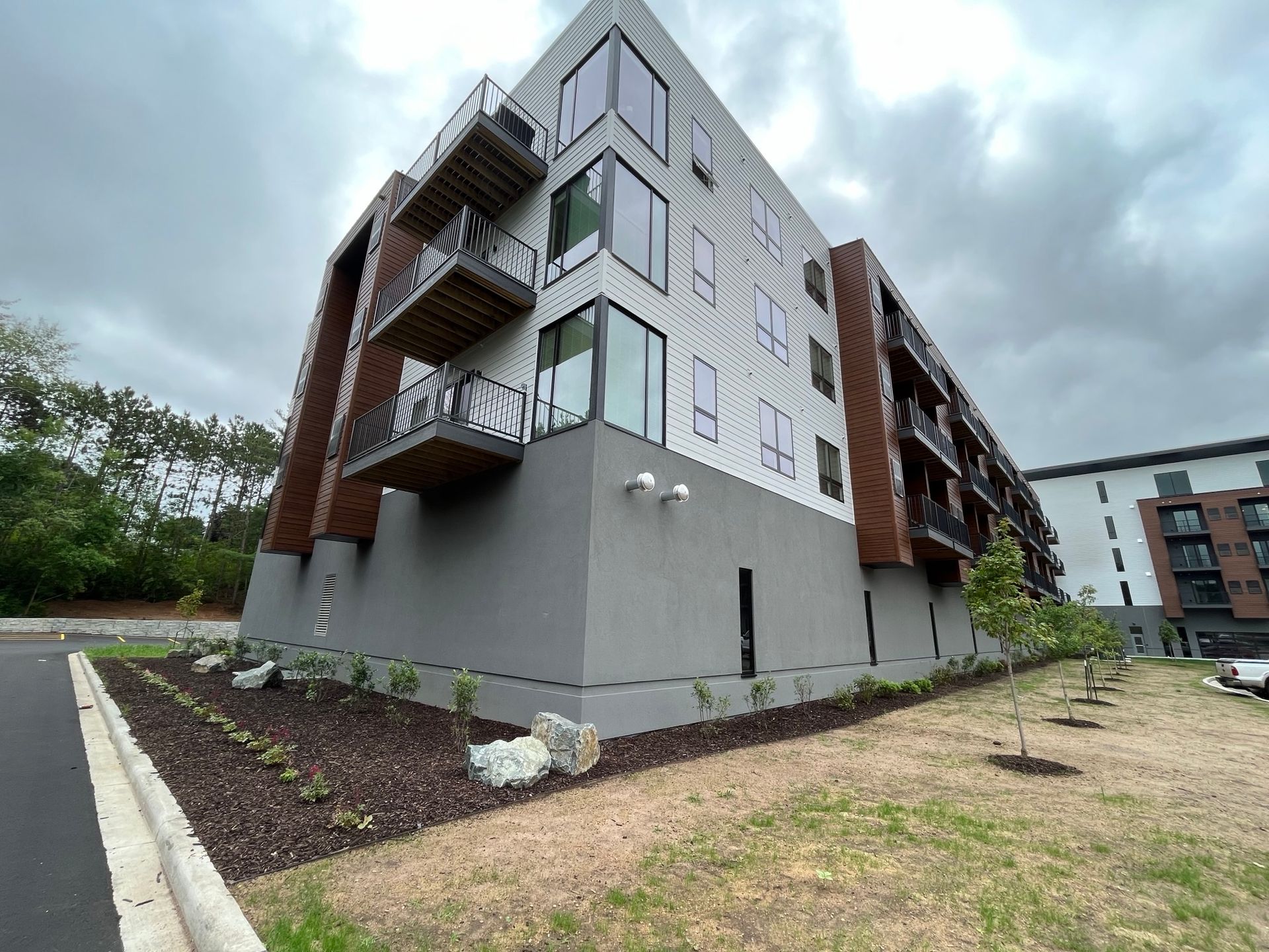 Modern multi-story building with balconies, gray and white facade, and landscaped area.