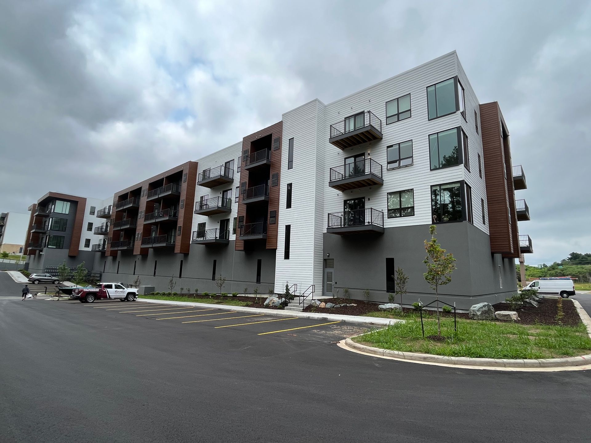Multi-story modern apartment building with metal and wood accents, balconies, and overcast sky.