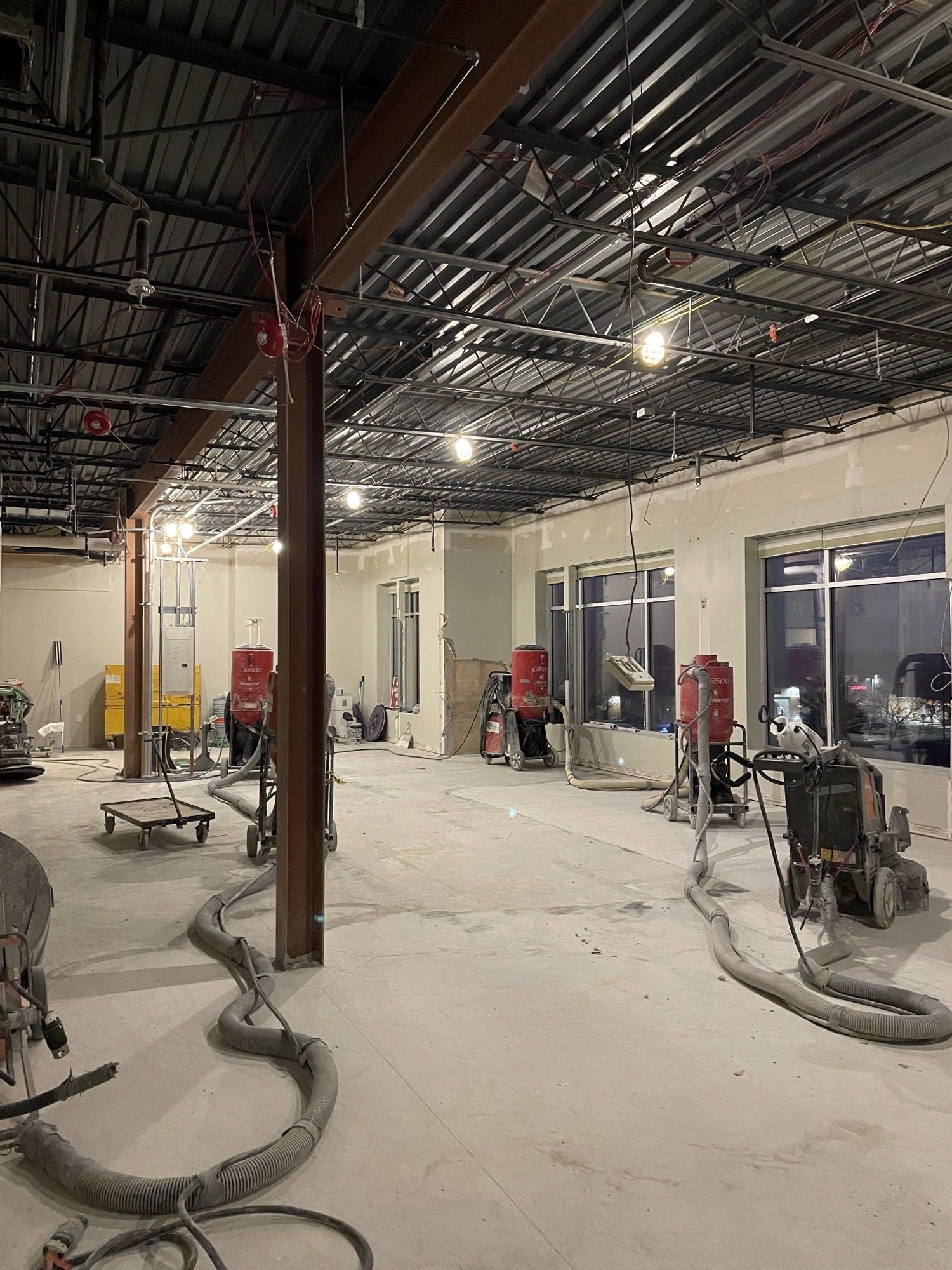 Construction interior with several floor grinders, exposed beams, and unfinished walls.