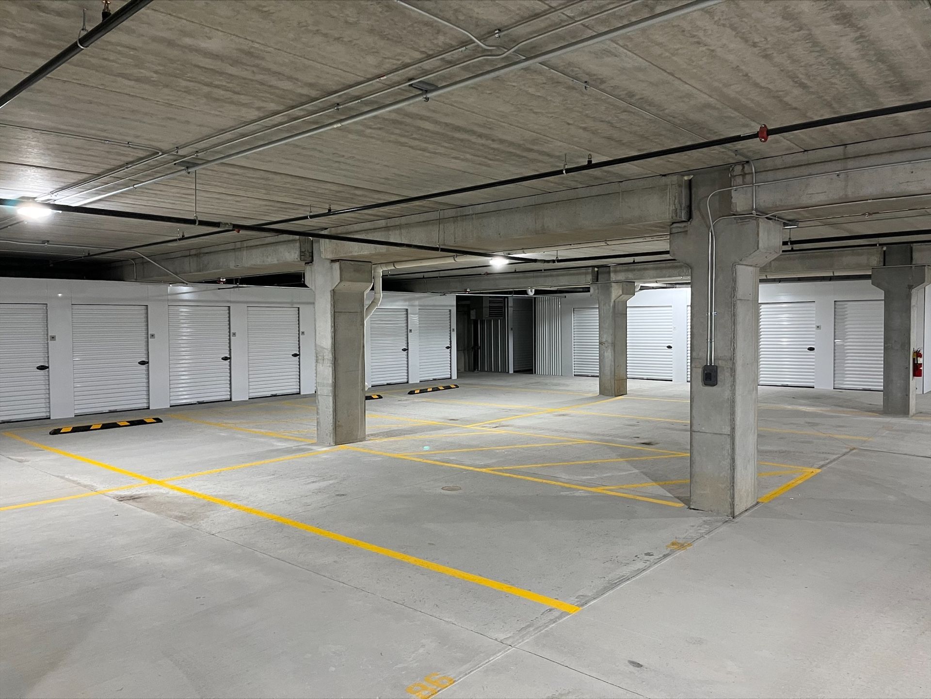Concrete parking garage with white storage units. Yellow lines mark parking spaces.