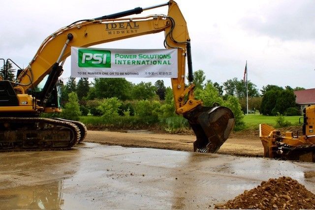 Yellow excavator digging on wet ground with a banner for Power Solutions International.
