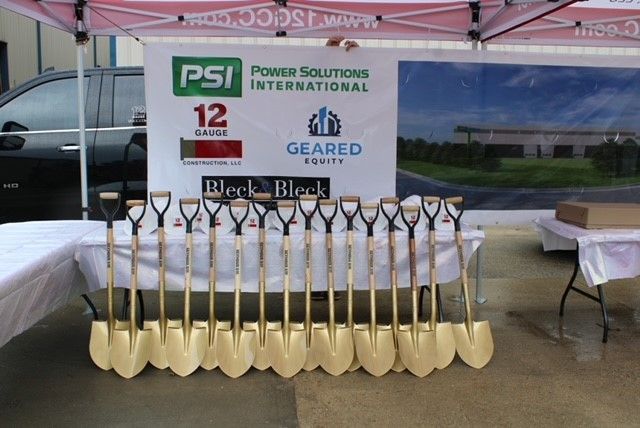 Golden shovels lined up in front of a banner for Power Solutions International, ready for a groundbreaking ceremony.