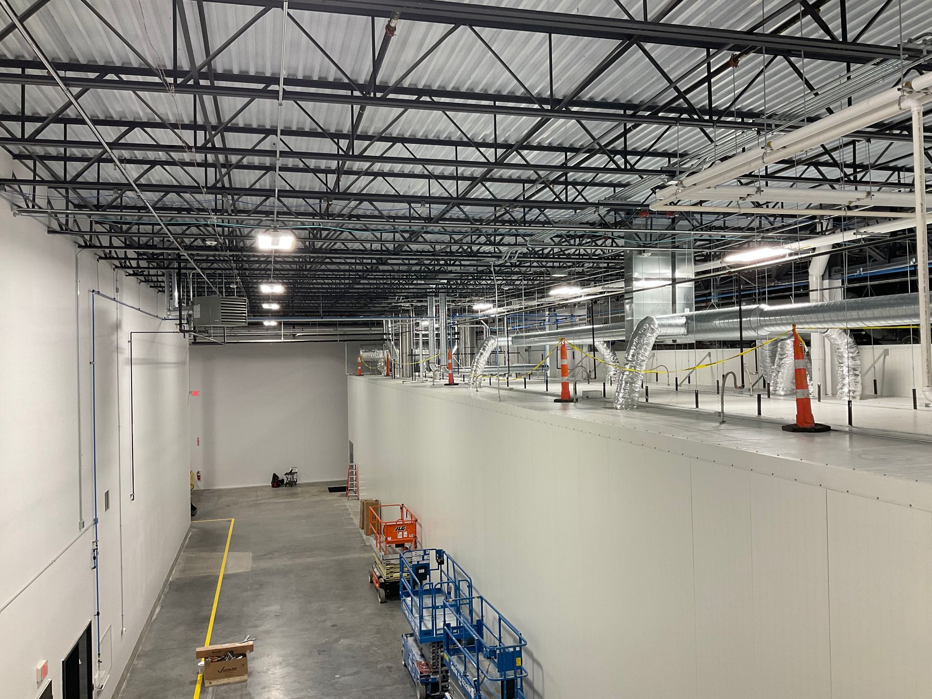 Interior view of a construction site. White walls and ceiling, visible metal beams, ductwork, and equipment.