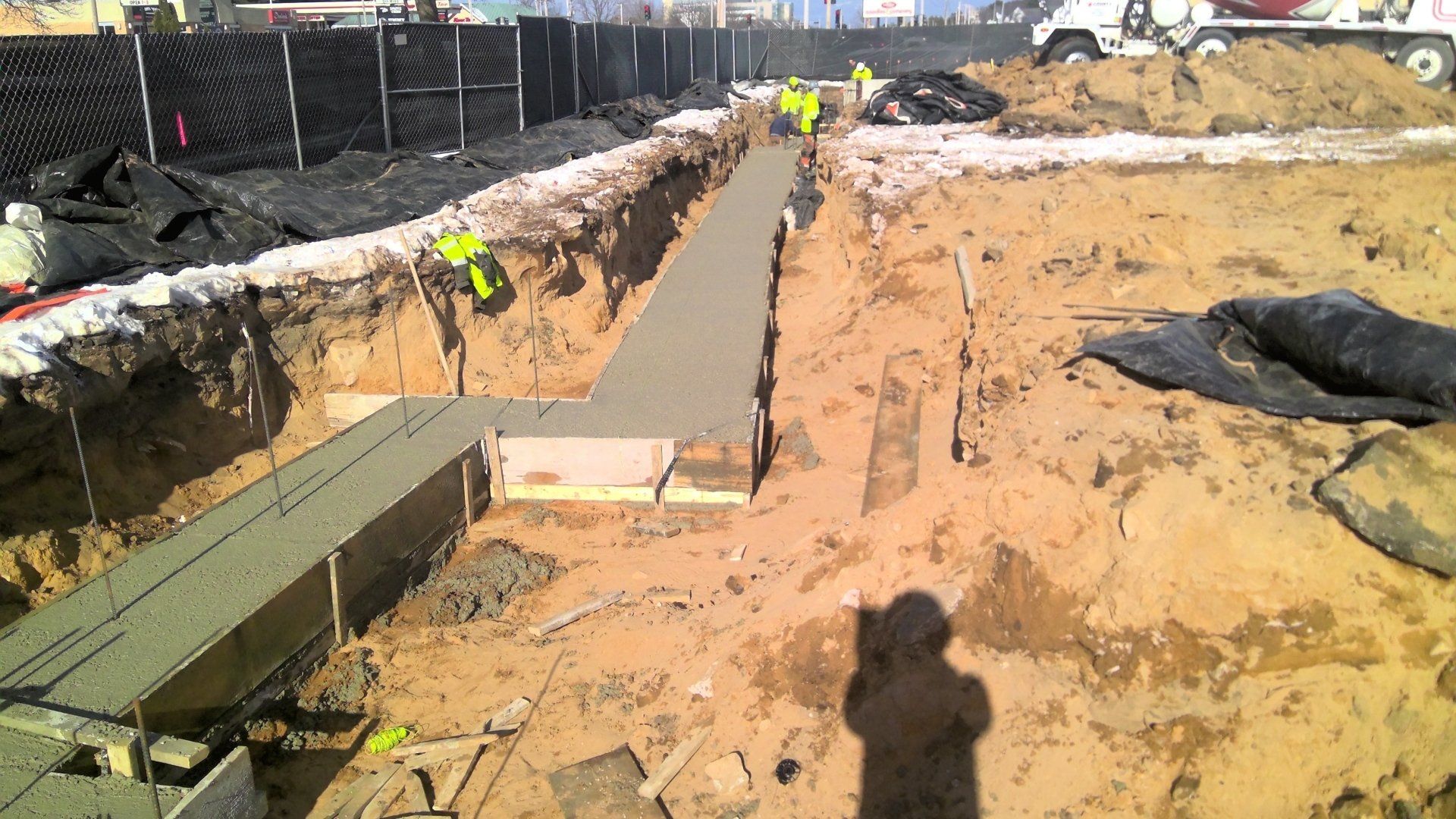 Construction workers pouring concrete foundation; a long trench with wet concrete.
