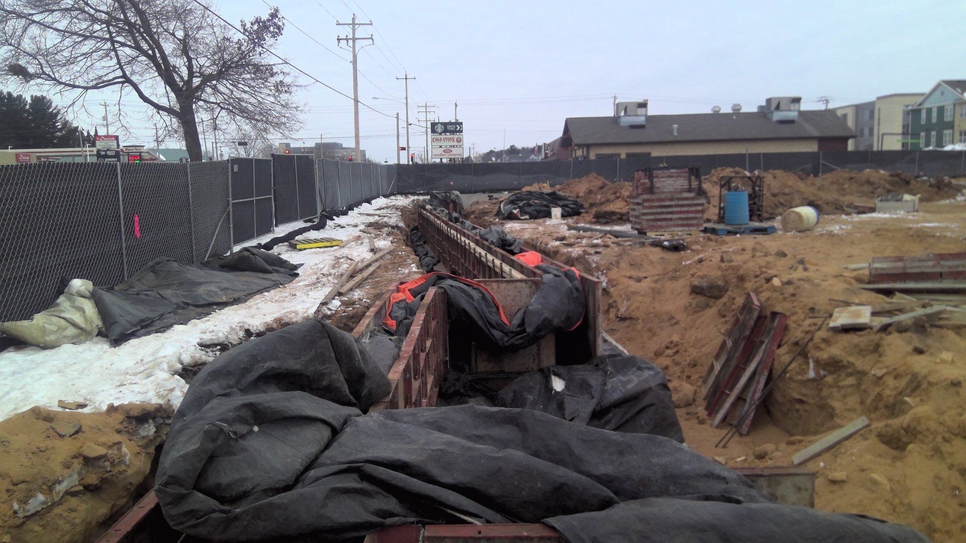 Construction site with a trench, fencing, and snow.