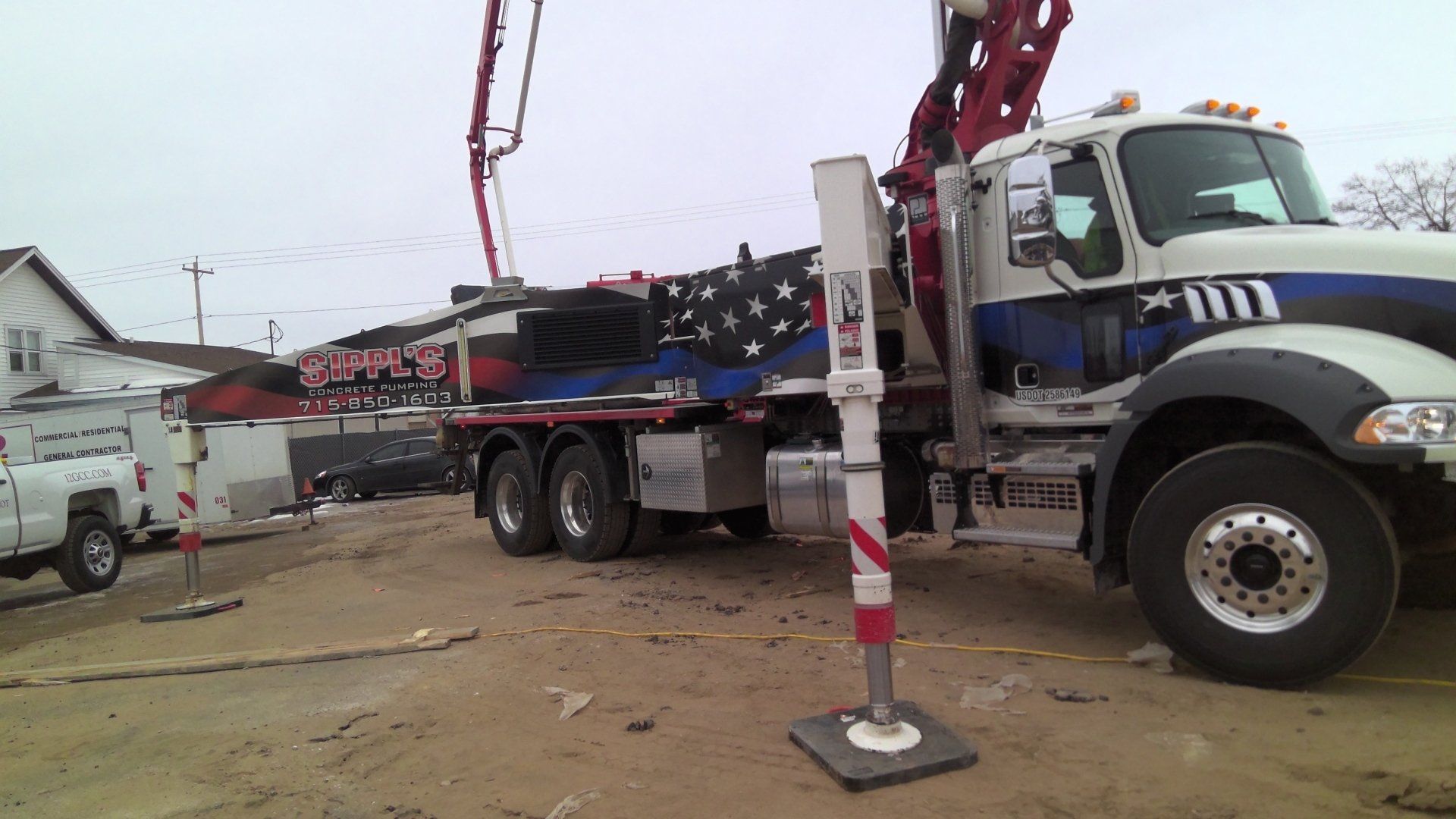 Concrete truck with raised boom pumping concrete at a construction site. Blue, white, and red design on the truck.