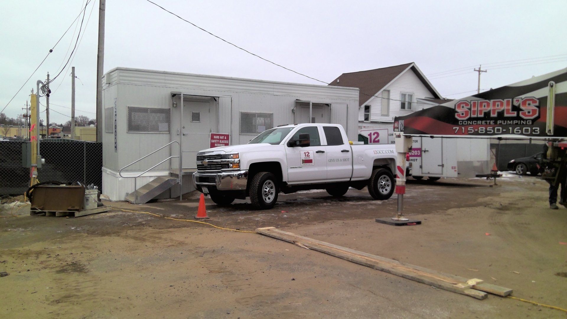White pickup truck parked outside a white building with construction equipment and a fence in an urban setting.