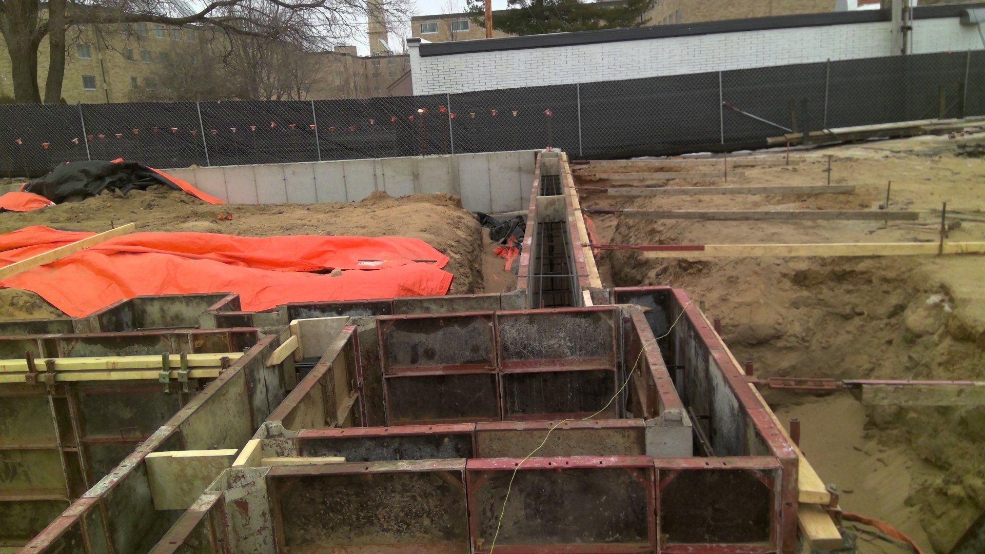 Construction site with concrete forms, orange tarp, and exposed earth.