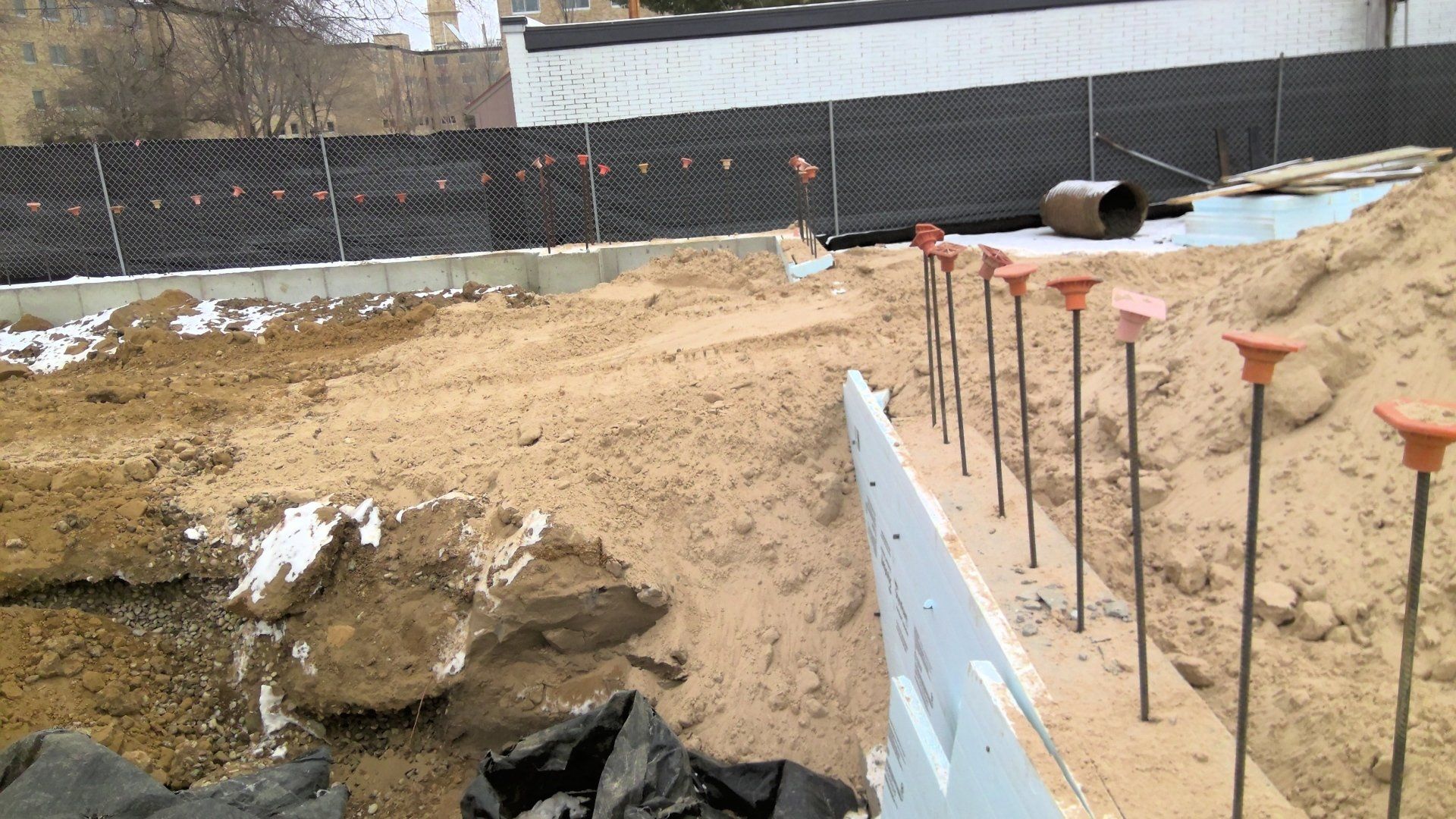 Construction site with sand, retaining wall, and metal stakes with orange caps.