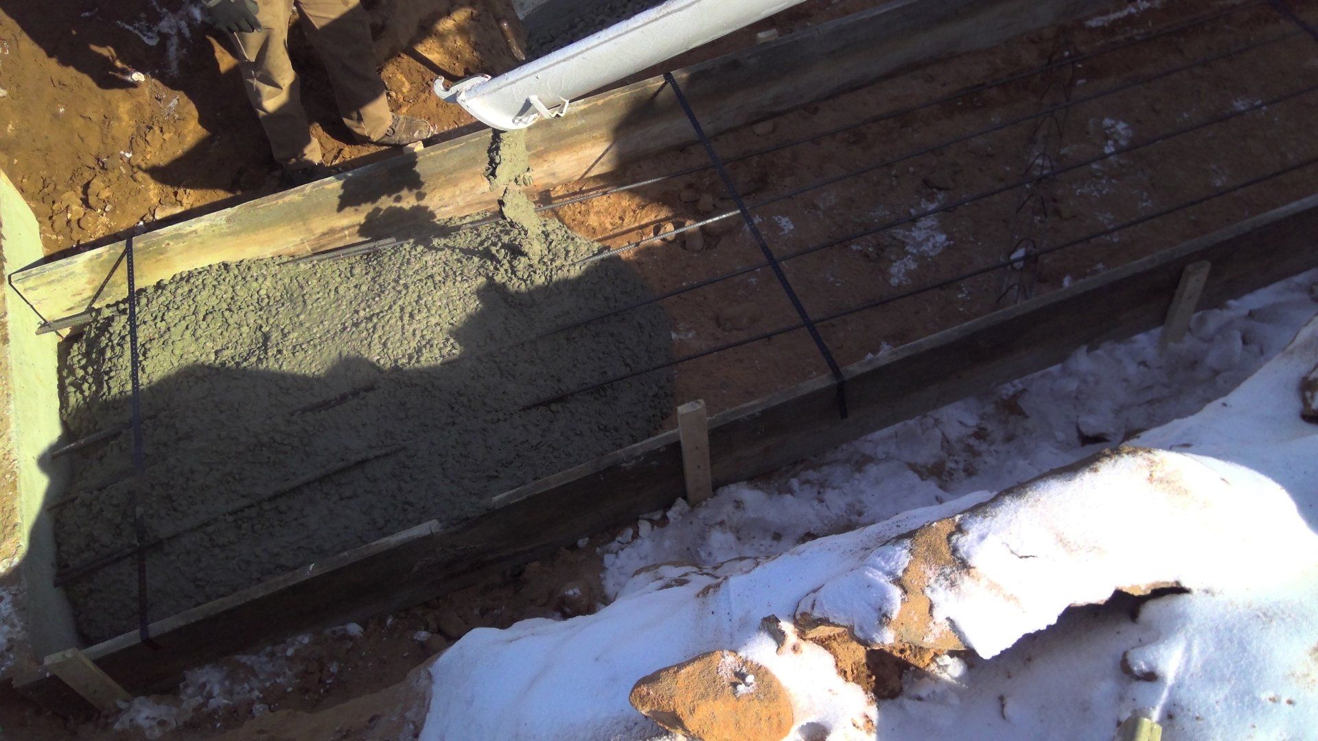 Concrete being poured into a wooden frame at a construction site.