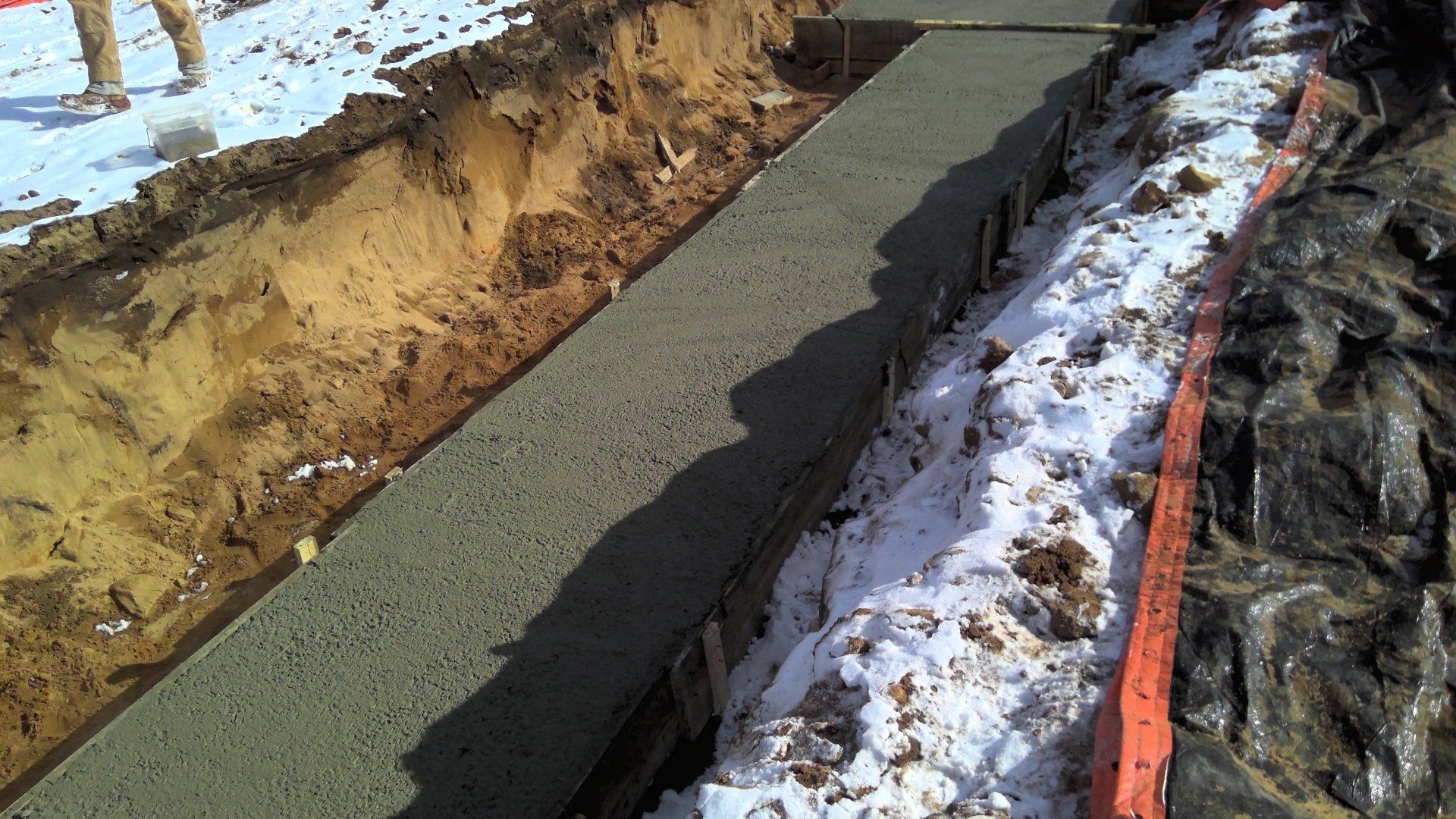 Concrete poured into a trench, likely for a foundation, with snow on either side.