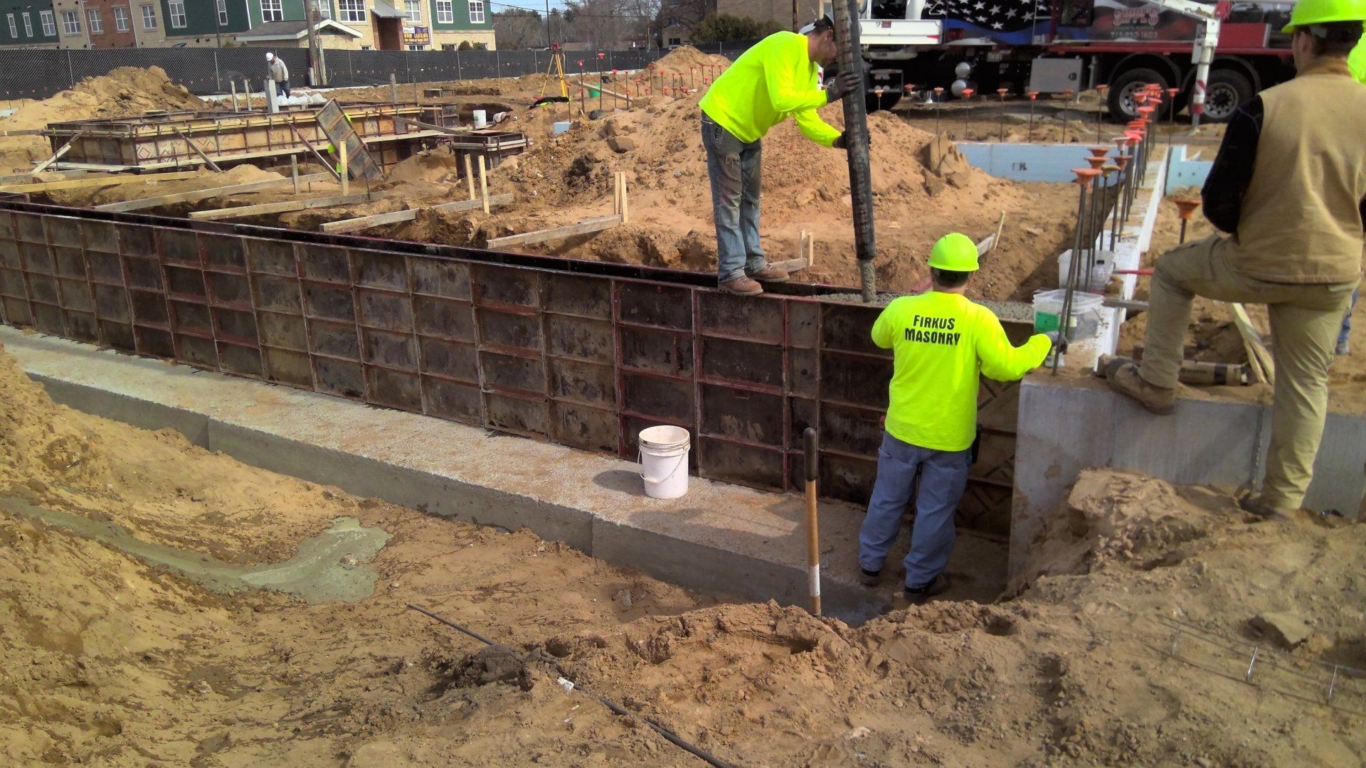 Construction workers pouring concrete into wall forms at a construction site.