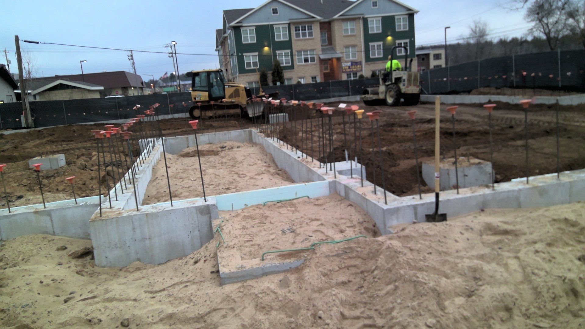 Construction site with concrete foundation walls, backhoes, and a building in the background.