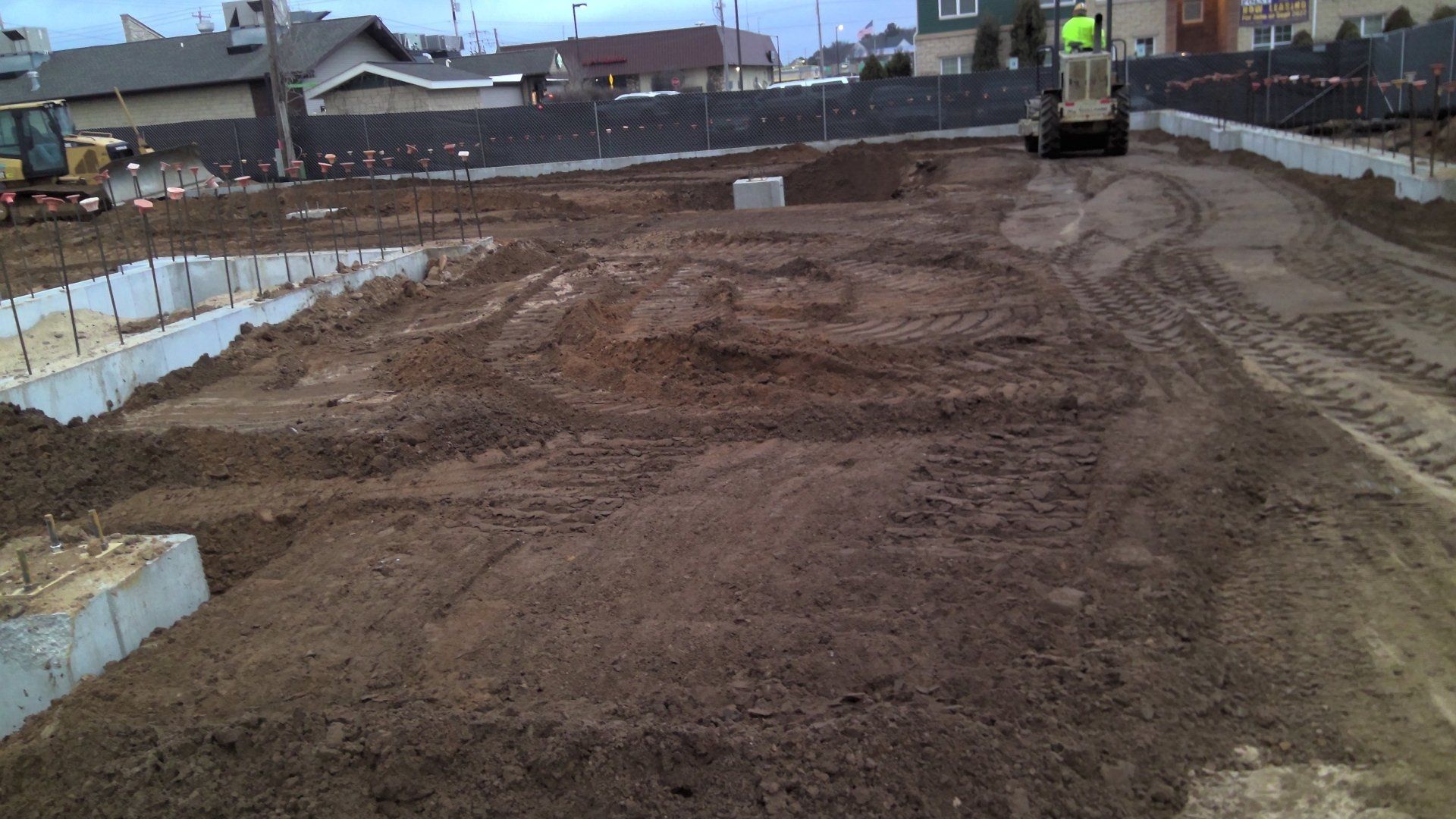 Construction site: Dirt pile, concrete foundation, machinery, and a fence.