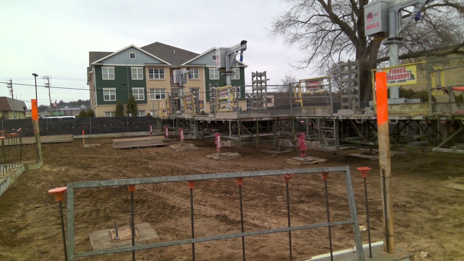 Construction site with dirt ground and a building under construction; orange safety markers.