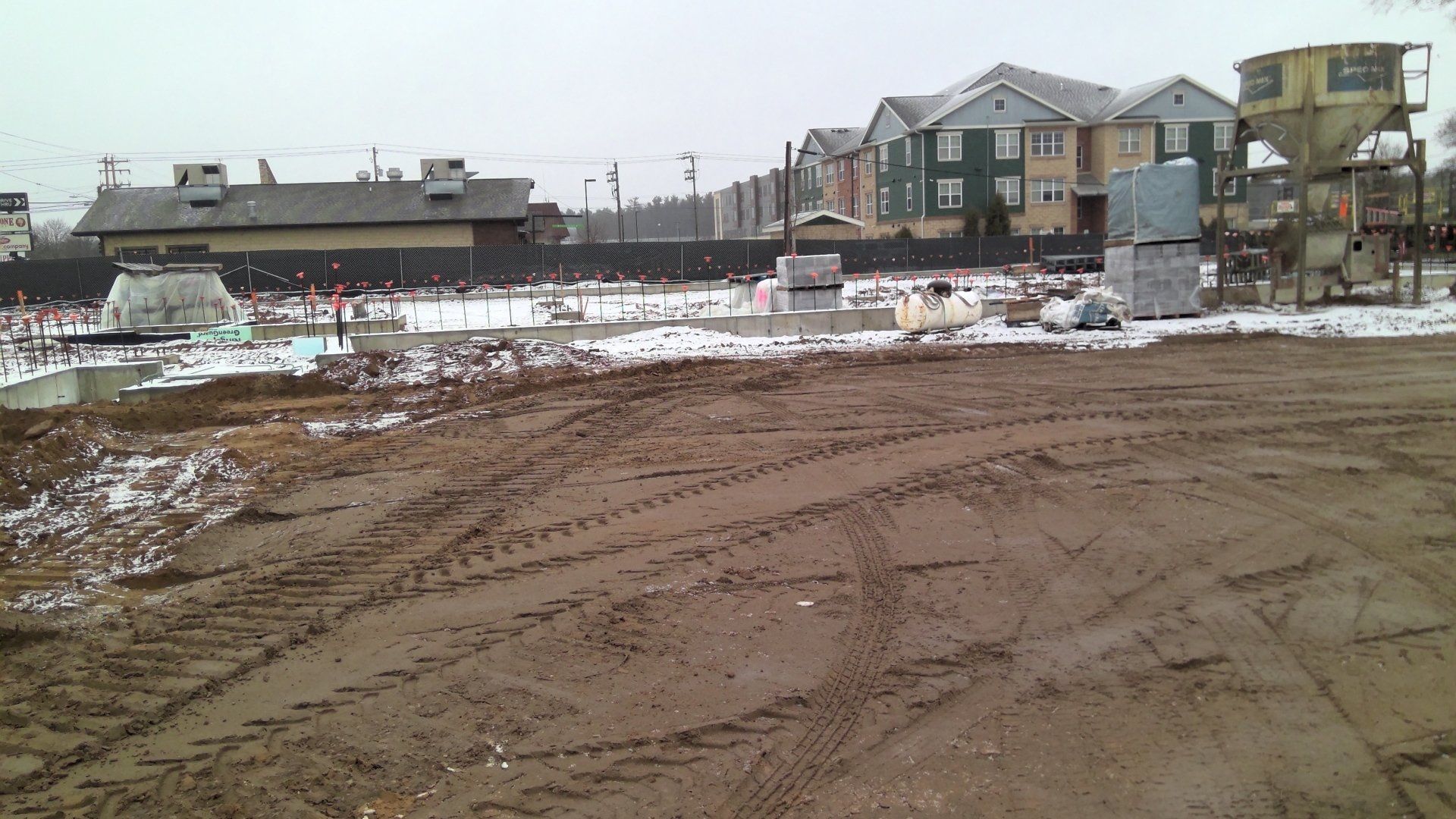 Construction site with mud, snow, and buildings in the background.