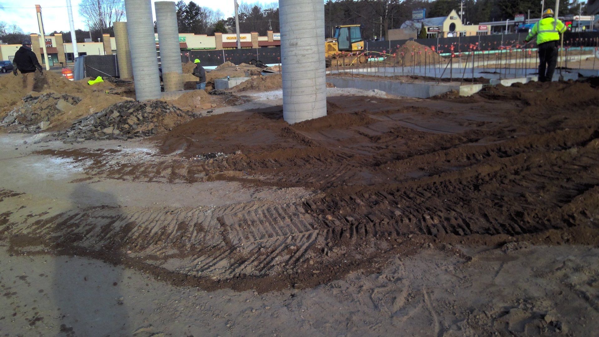 Construction site with cylindrical pillars, dirt, and workers.