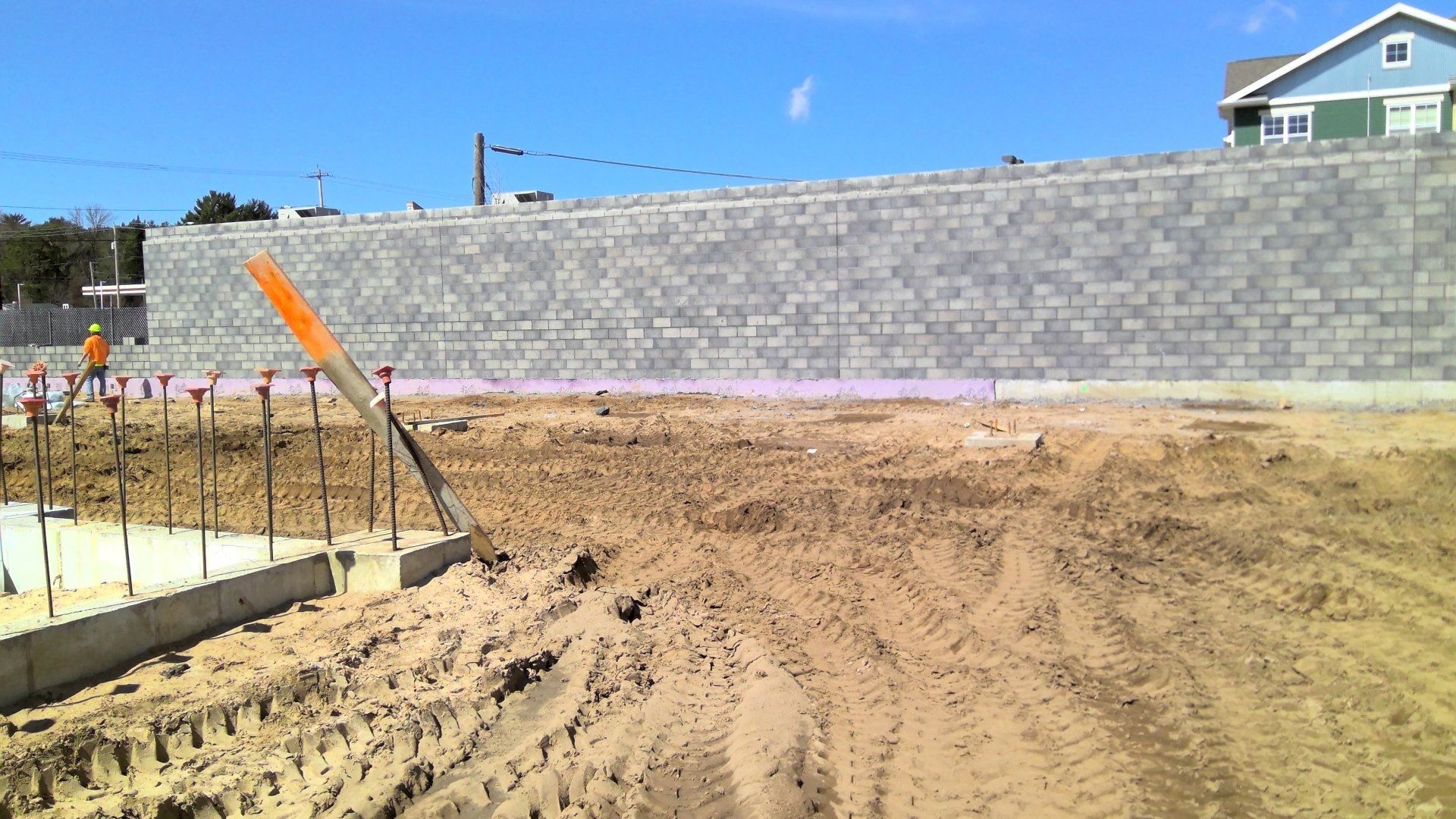 Construction site: unfinished concrete foundation, gray block wall, dirt, blue sky.