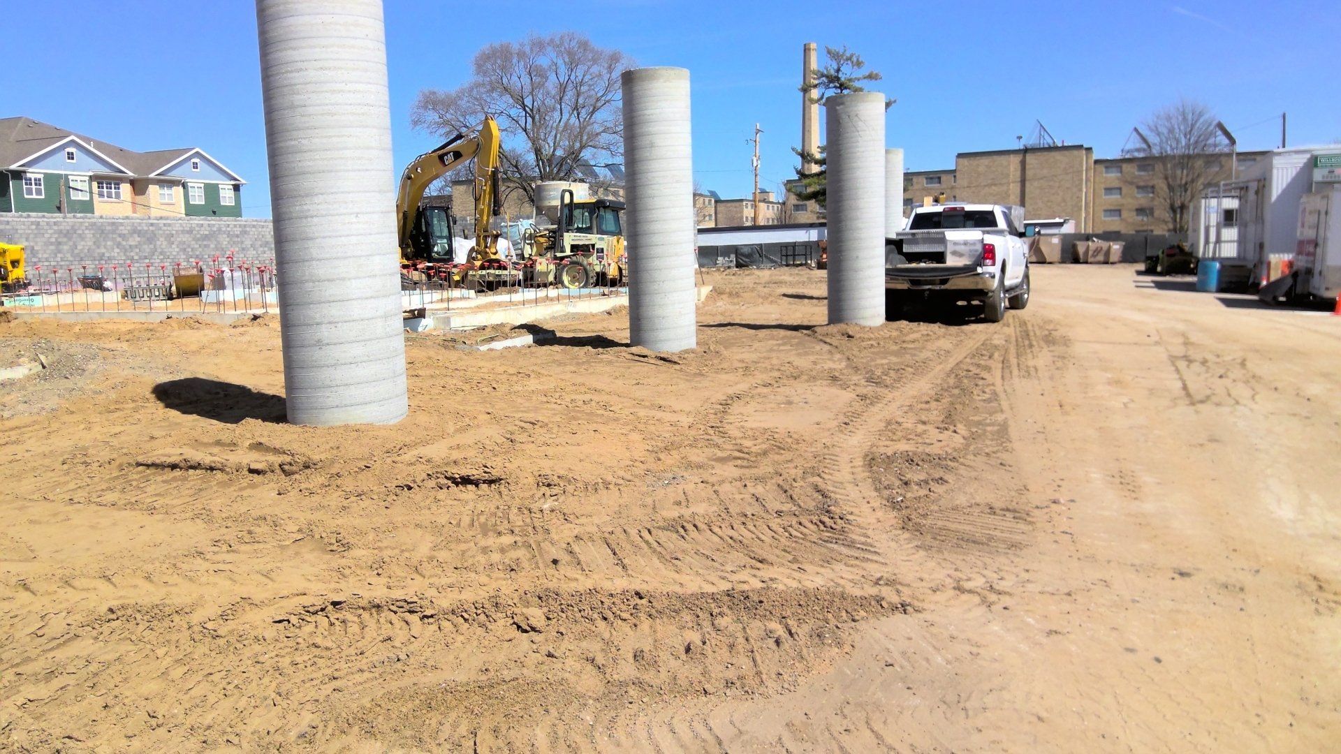 Construction site with concrete pillars and heavy machinery. A white pickup truck is parked nearby.