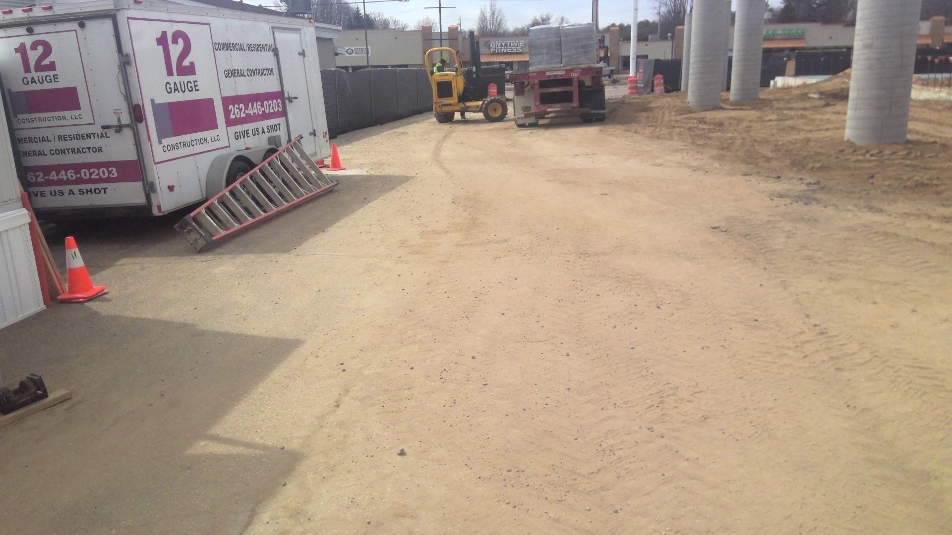 Construction site with a white truck, a ladder, a forklift, and concrete pillars.